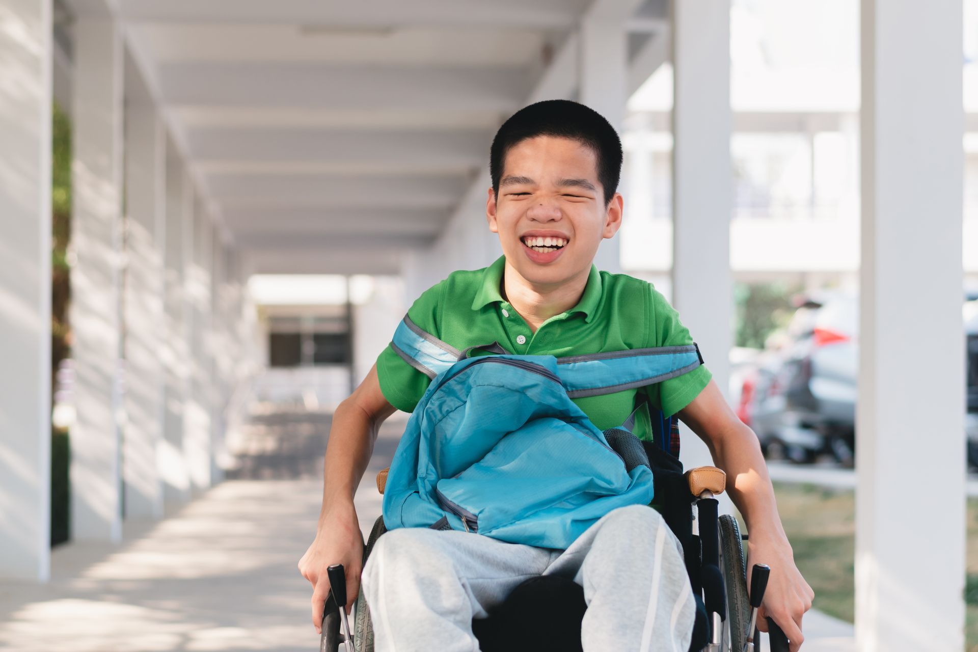 Child with CP with school backback on lap in wheelchair smiling