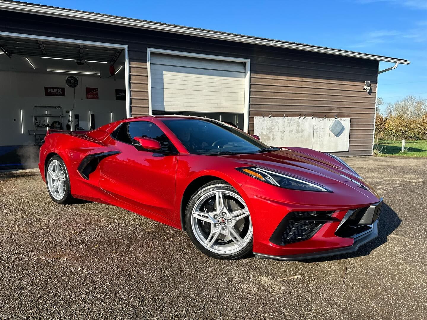 Red Chevrolet Corvette sports car parked outside a wooden garage on a sunny day.