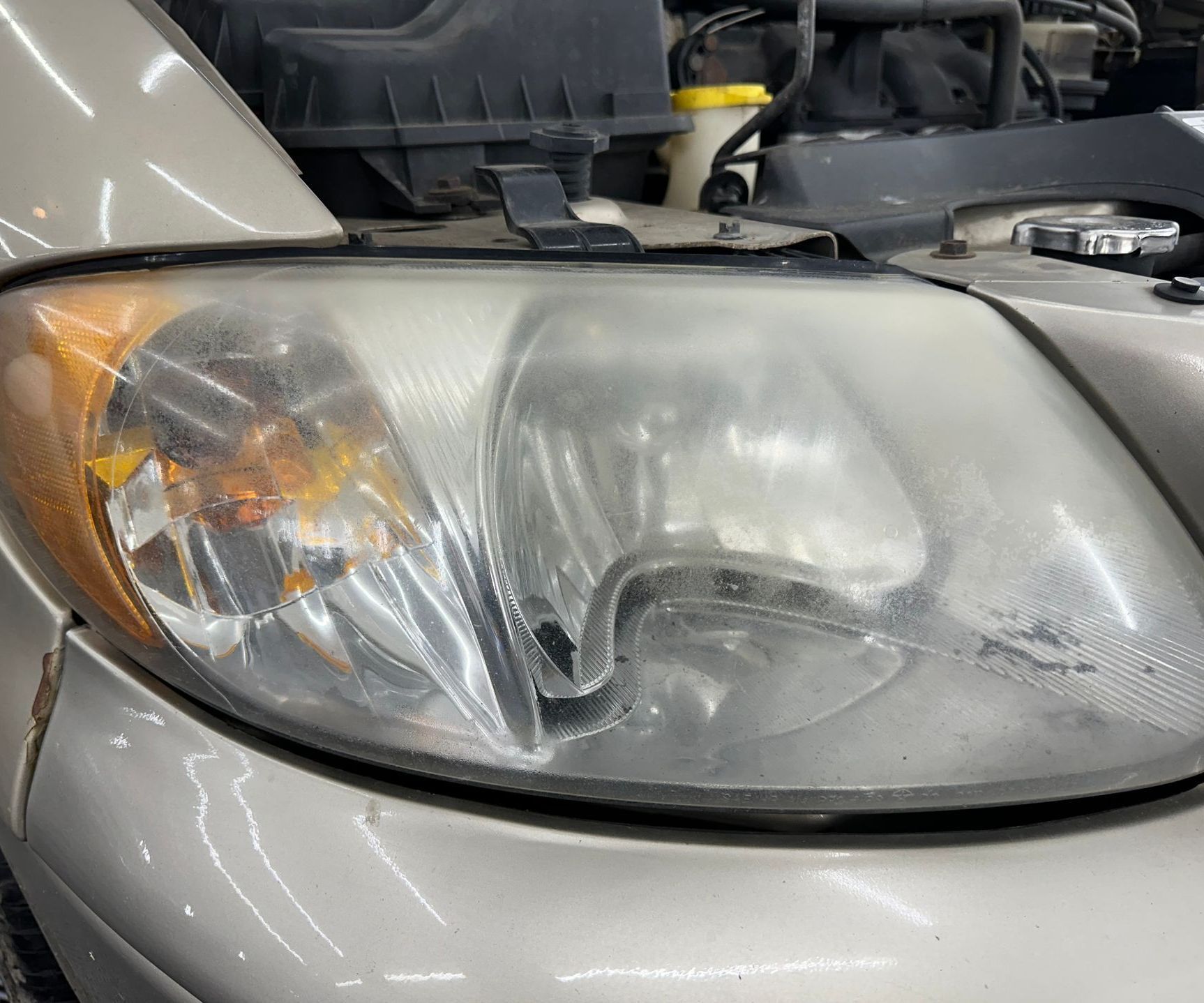 A close up of a car 's headlight with the hood open.