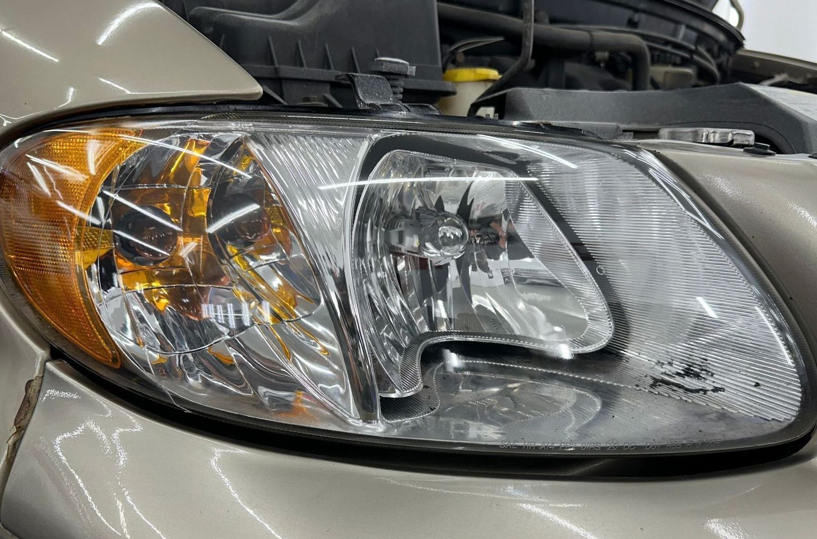 A close up of a car headlight with the hood open.