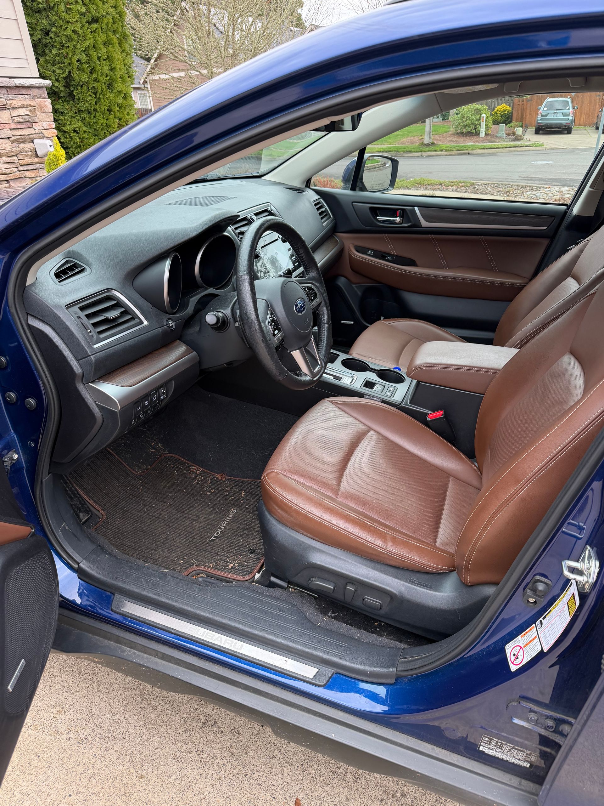 Interior of a blue Subaru Outback with brown leather seats and a black steering wheel.