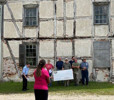 Group of people holding a large check in front of a historic building.