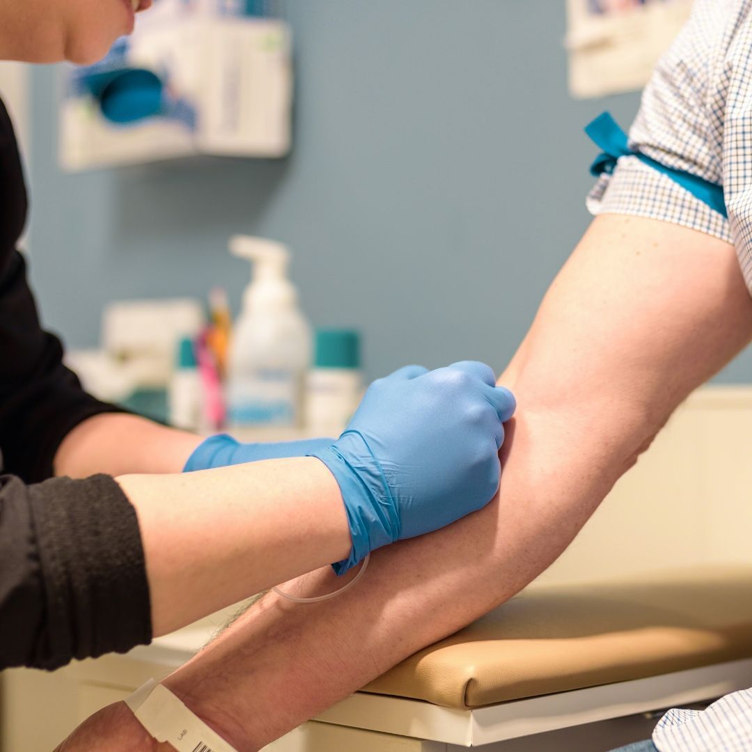 A medical professional drawing blood from a patient's arm in a doctor's office.