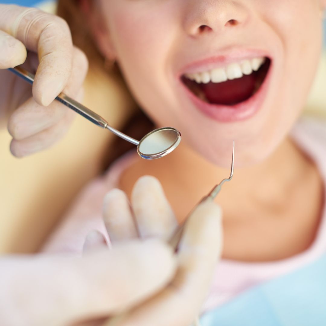 Dentist examining a patient's mouth with a mirror and probe; person smiles.