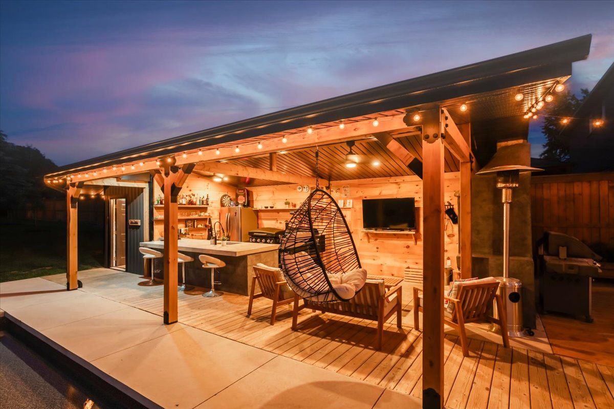 A wooden gazebo with a wicker chair underneath it is lit up at night.