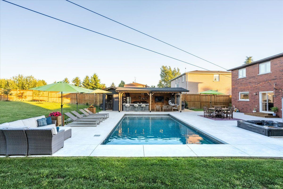 A large swimming pool surrounded by chairs and umbrellas in a backyard