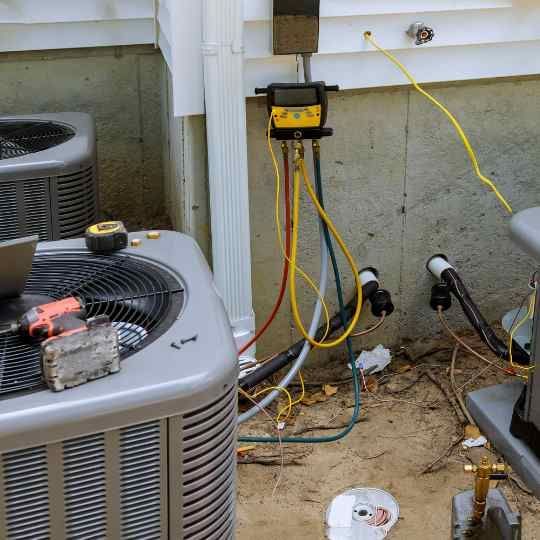 HVAC technician servicing an air conditioning unit; hoses and gauges connected to the unit.