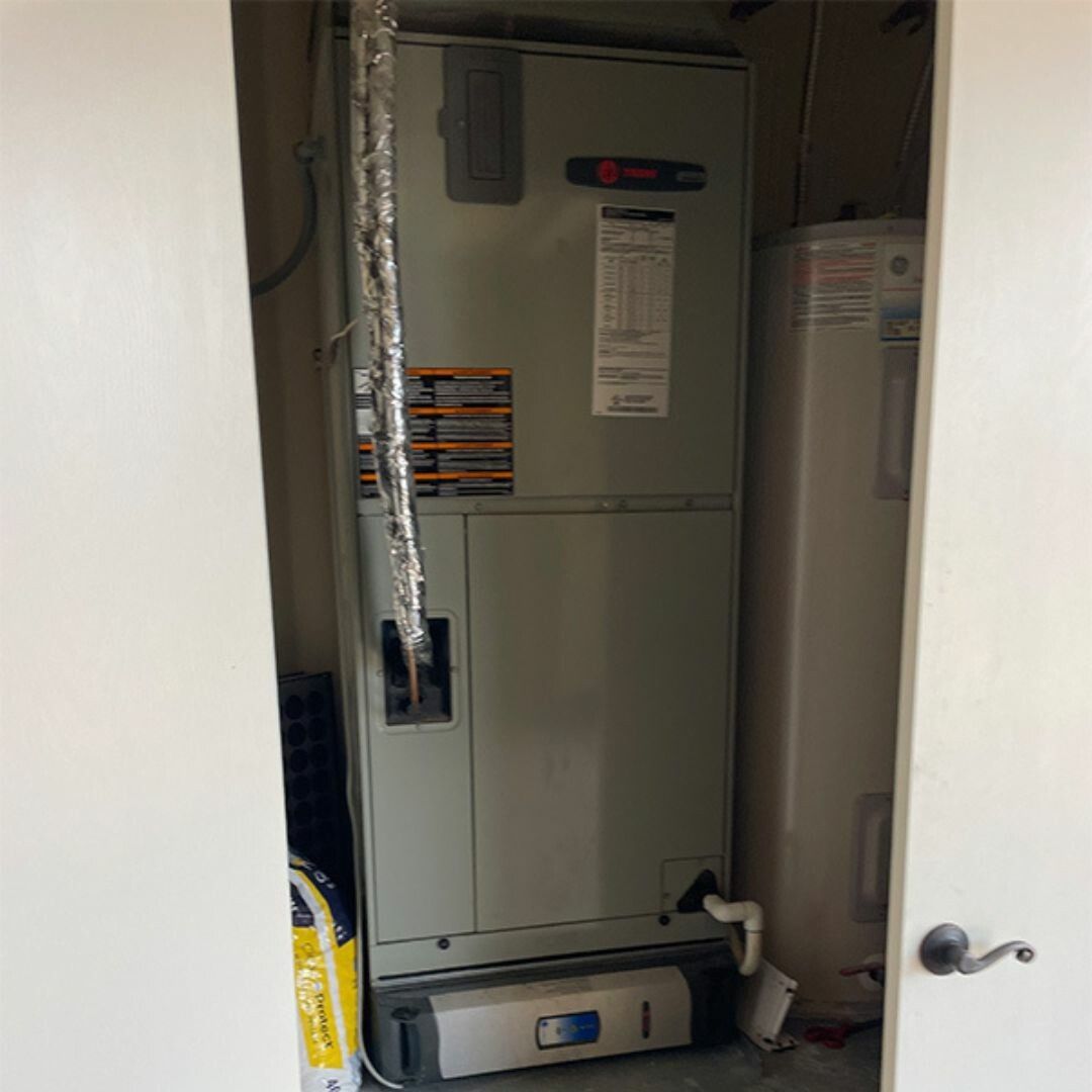 HVAC unit and water heater in a closet, viewed through open white doors. Silver insulated pipe visible.