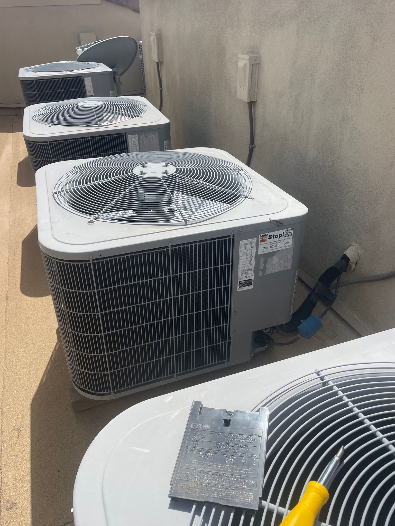 Air conditioning units lined up on a rooftop. A person may be repairing one.