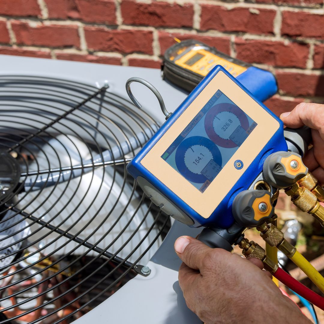 HVAC technician using a digital manifold gauge on an outdoor air conditioning unit.