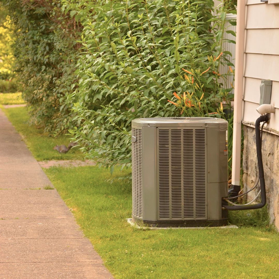 Air conditioning unit on a grassy lawn next to a sidewalk and a building.