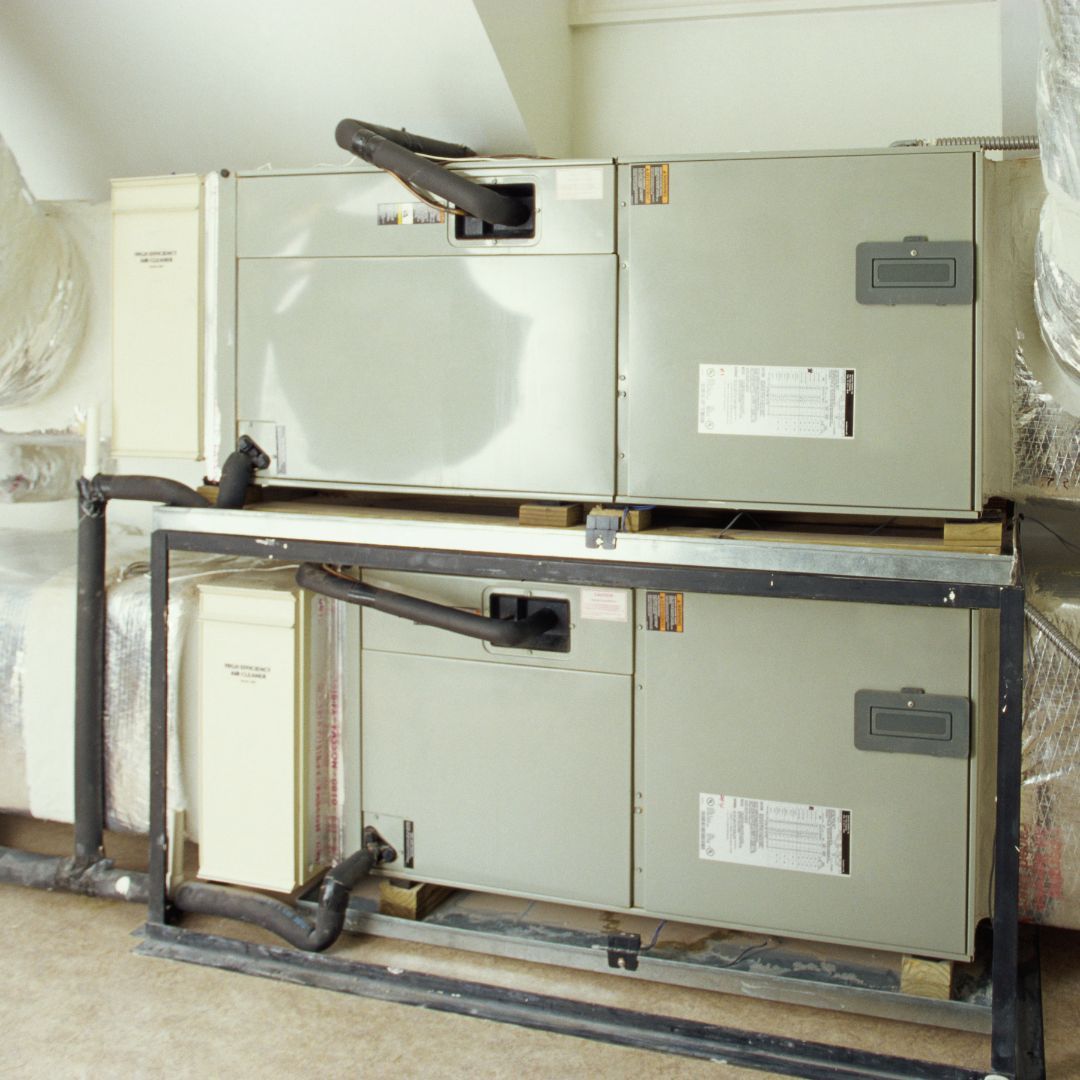 Two HVAC units stacked in an attic, with black pipes and ductwork.