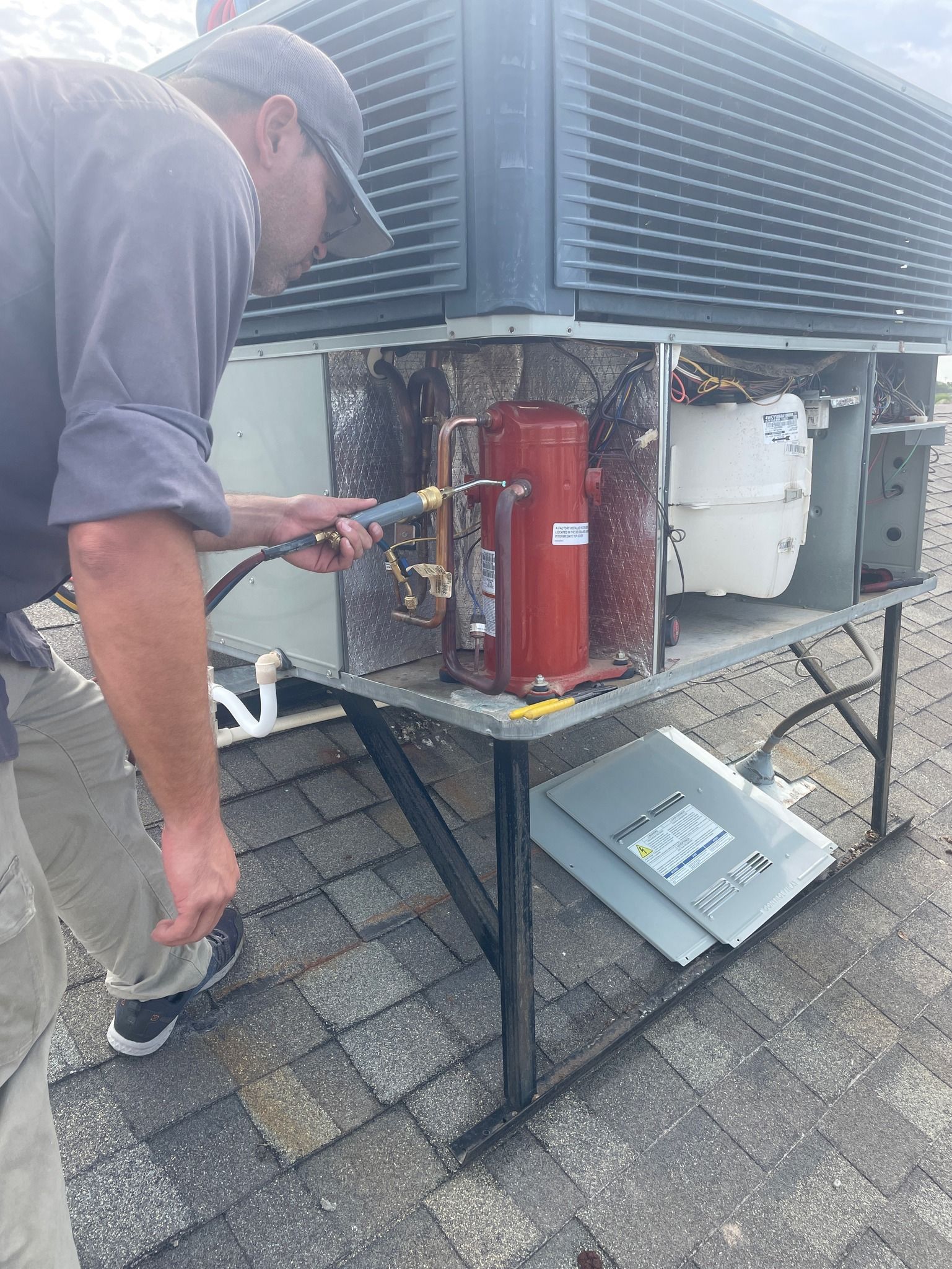 HVAC technician cleans an air conditioning unit on a rooftop. He uses a spray nozzle.