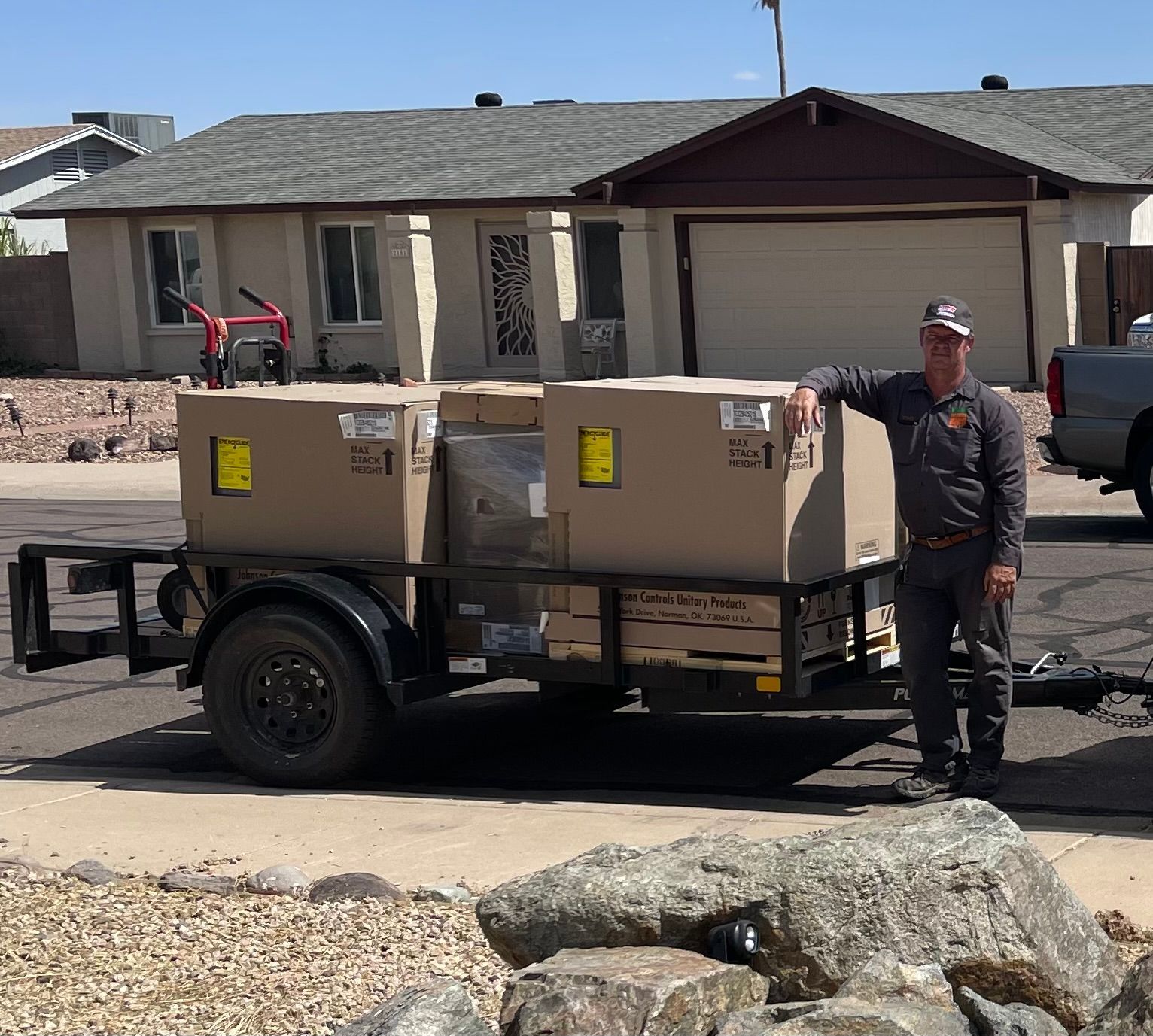 Man standing beside a trailer loaded with large boxes in front of a house.