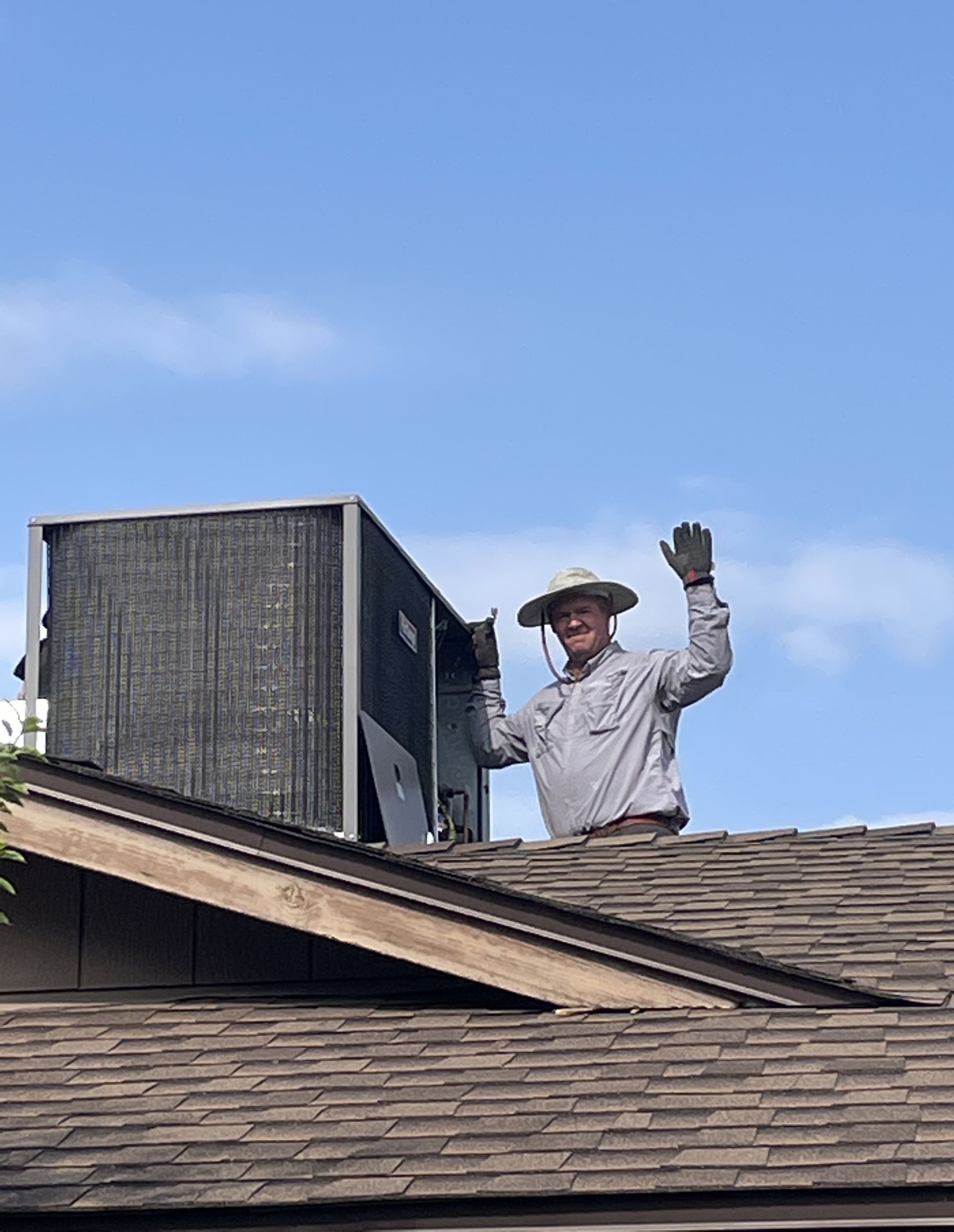 Man waves from rooftop next to air conditioning unit, blue sky.