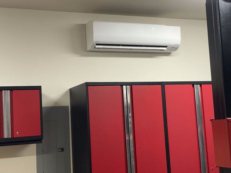 White air conditioner on beige wall above red storage cabinets.