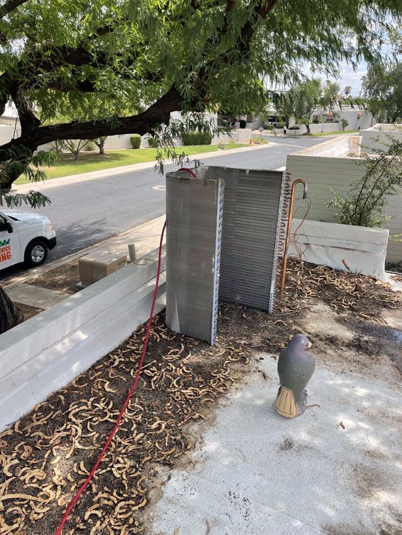 Two gray air conditioning coils on a concrete pad near a street and a white work van.