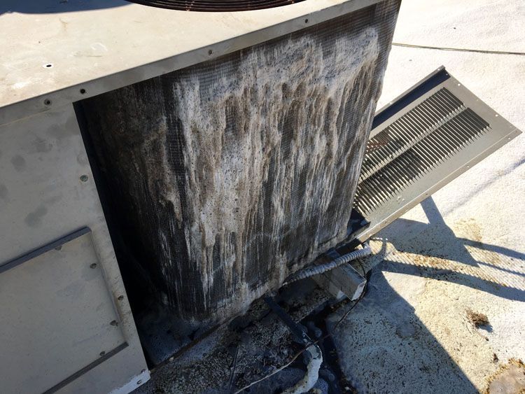Air conditioning unit, outdoor setting, with significant discoloration and buildup on the metal components.