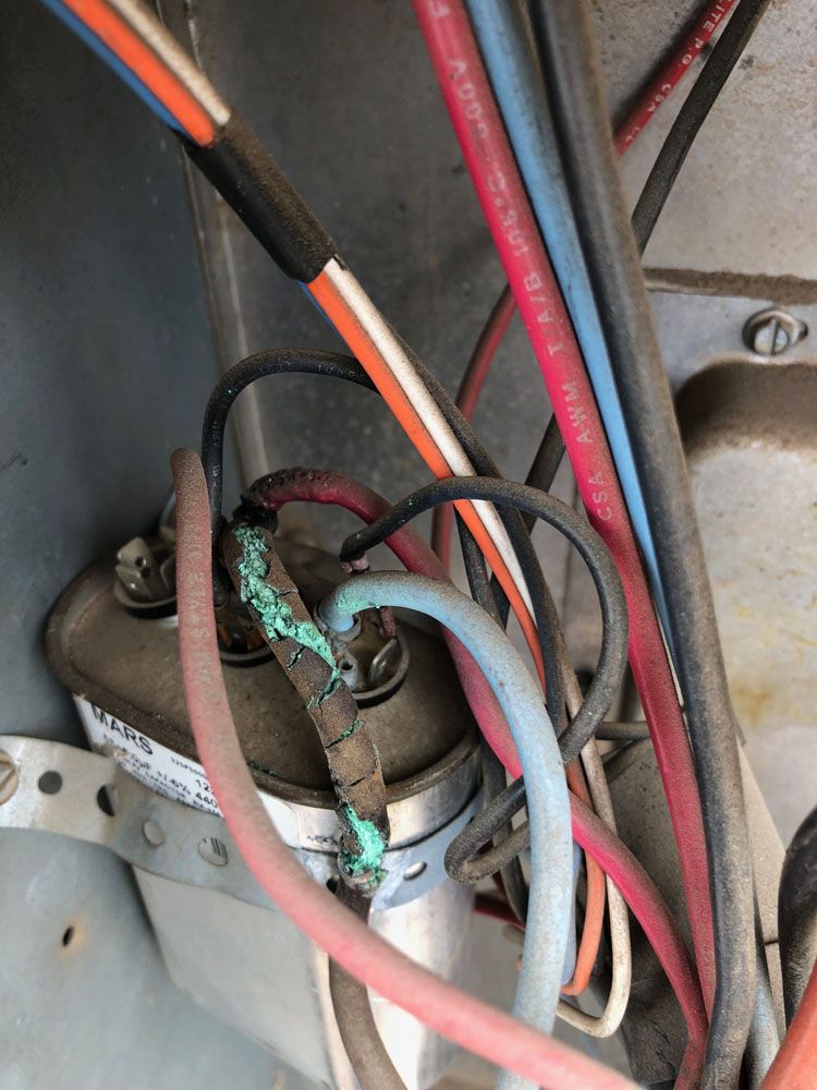Close-up of an AC capacitor with corroded terminals and connected wires of various colors.