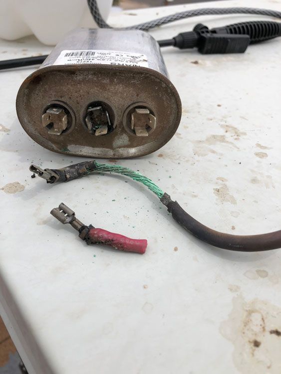 Damaged capacitor with burnt wiring on a white surface, likely electrical equipment repair.