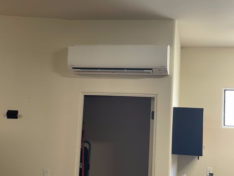 White ductless air conditioner mounted on a beige wall above a doorway.