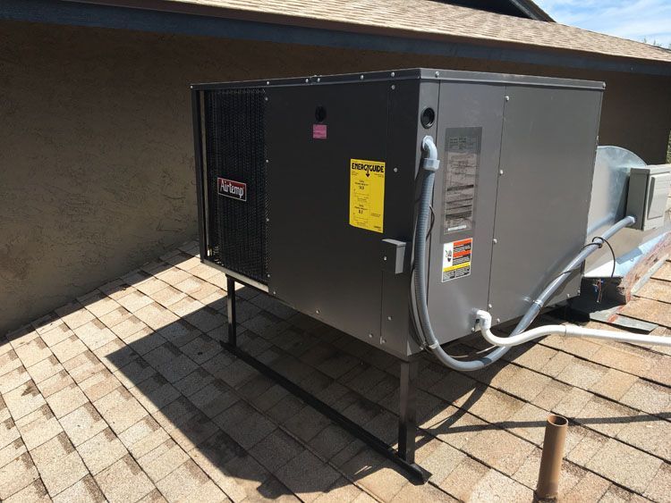Rooftop HVAC unit on a shingled roof, cast in sunlight, with a metal stand.
