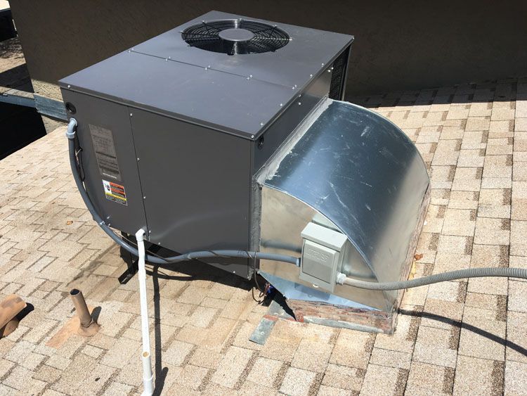 Rooftop HVAC unit, gray metal, with fan and ductwork, on a tiled roof.