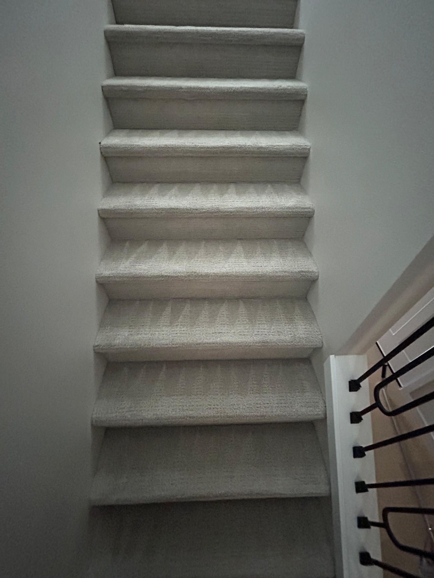 A set of carpeted indoor stairs with light gray carpet and white walls, viewed from the top looking down.