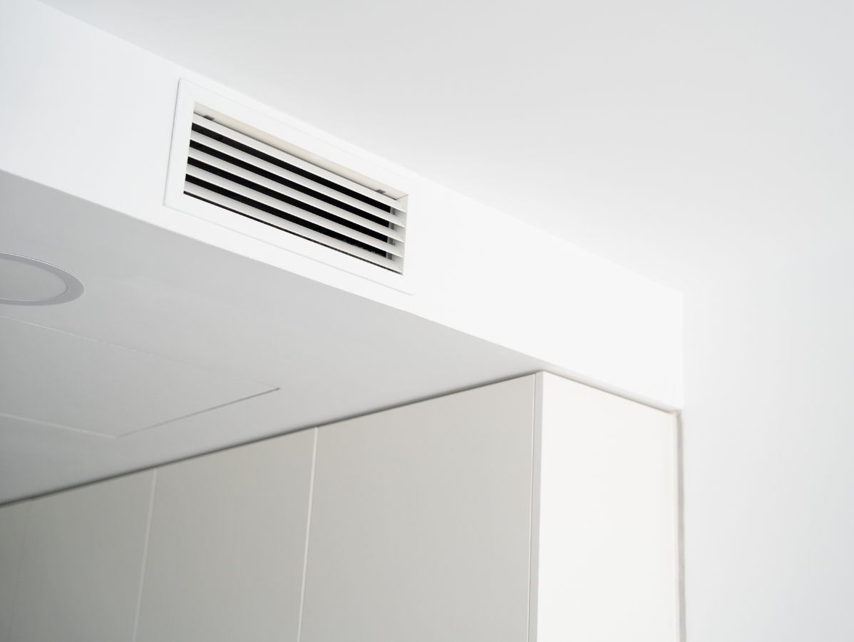 A rectangular HVAC ventilation grille integrated into a white ceiling bulkhead above a plain wall.