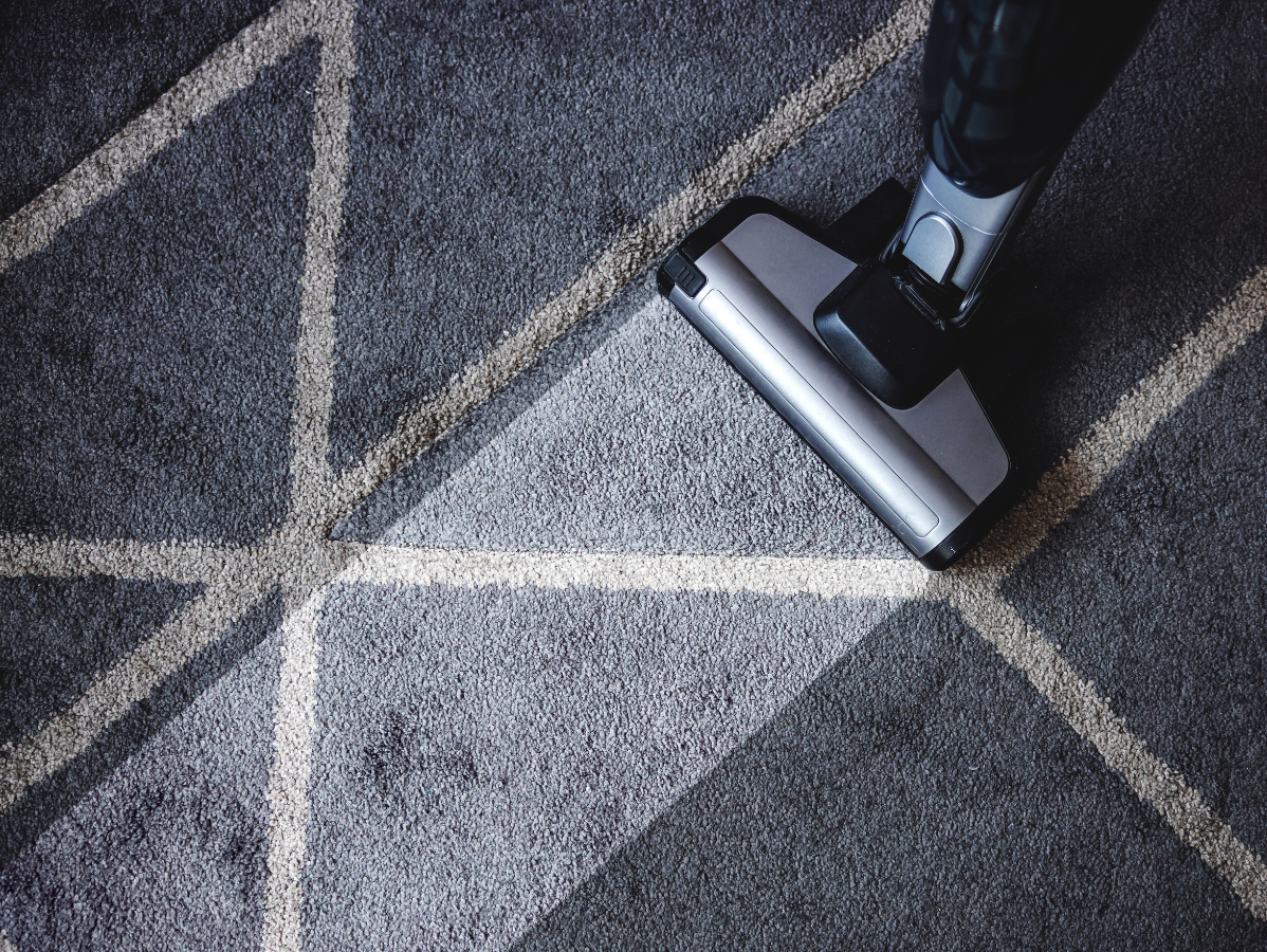 A vacuum cleaner head cleans a path across a dark, geometric patterned rug.