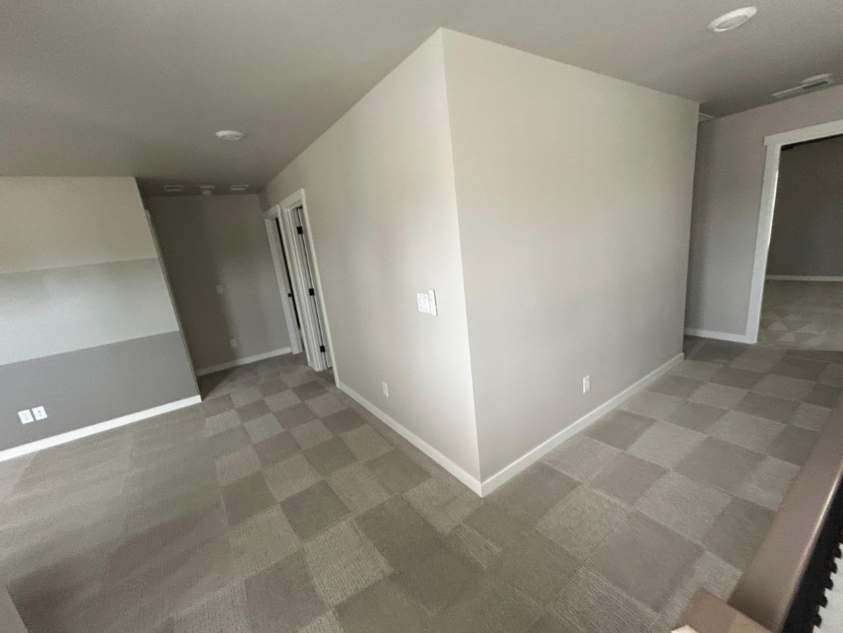An interior view showing a hallway with light-colored carpet and walls, leading to doorways on the left and right.