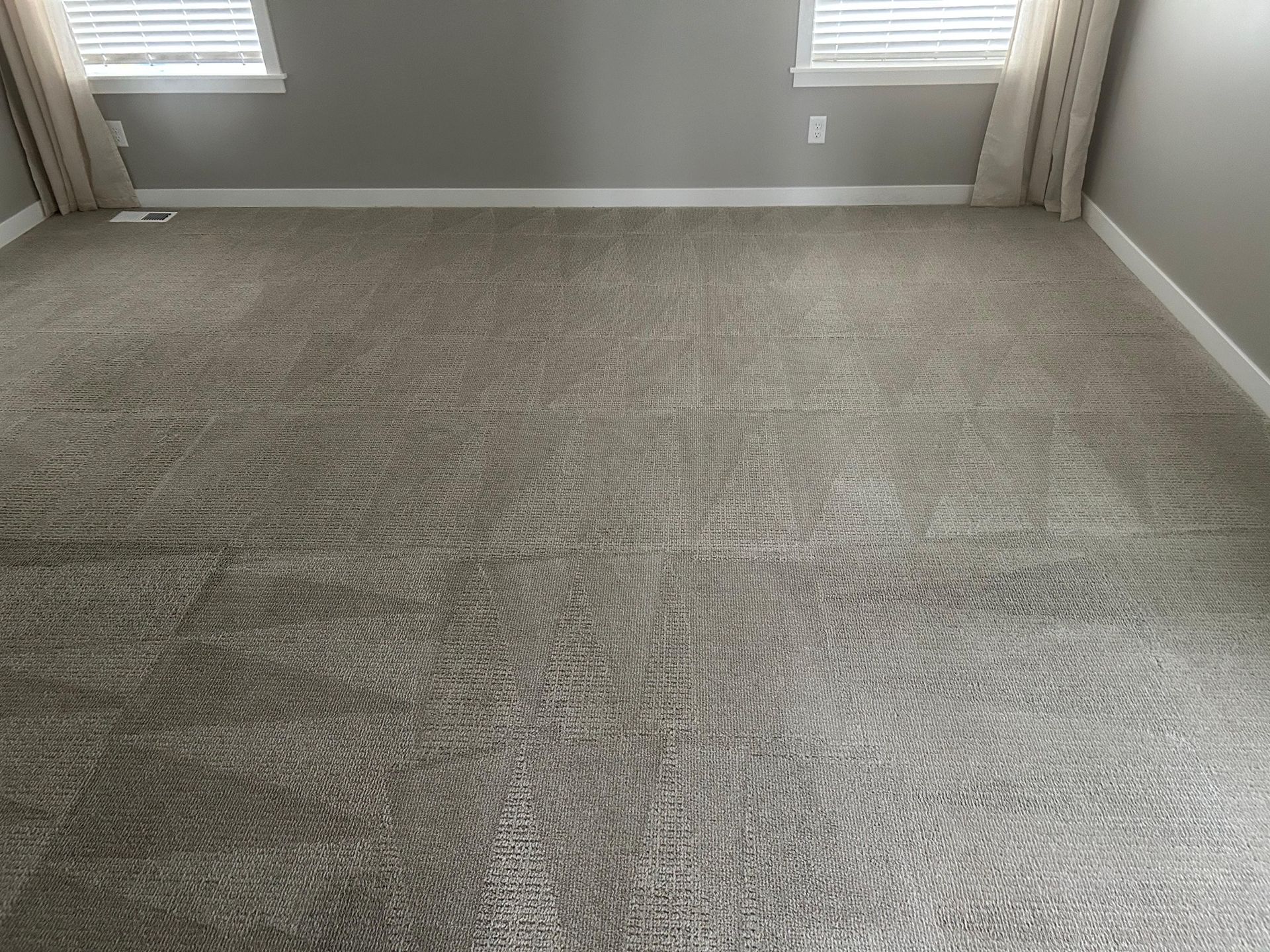 A grey, wall-to-wall carpeted room with two windows and beige curtains against a grey wall.