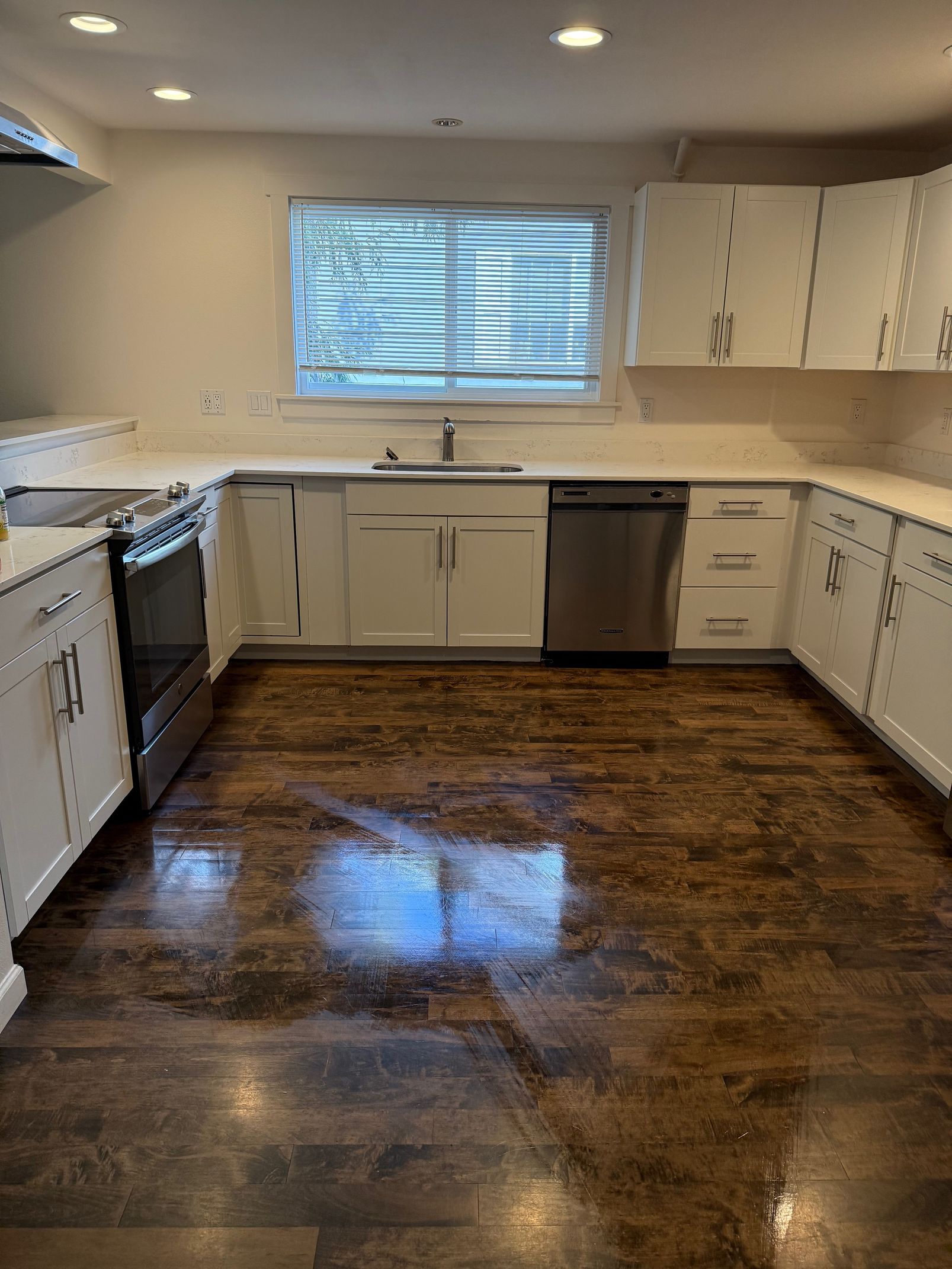 A bright kitchen with white cabinets, stainless steel appliances, a window above the sink, and dark wood-look flooring.