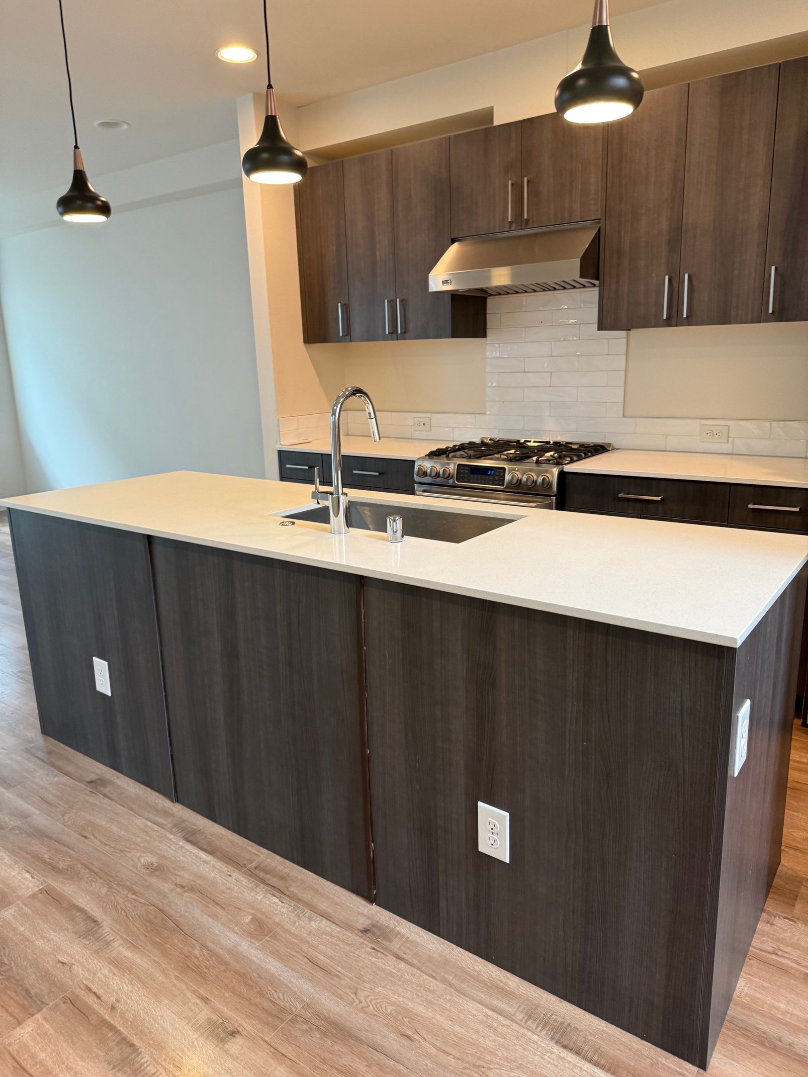 A kitchen island with dark wood cabinets and a white countertop, featuring a sink, faucet, and three pendant lights above.