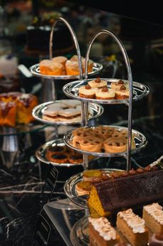Um suporte de metal de vários andares exibe uma variedade de doces, incluindo cupcakes, tortas e fatias retangulares de bolo.