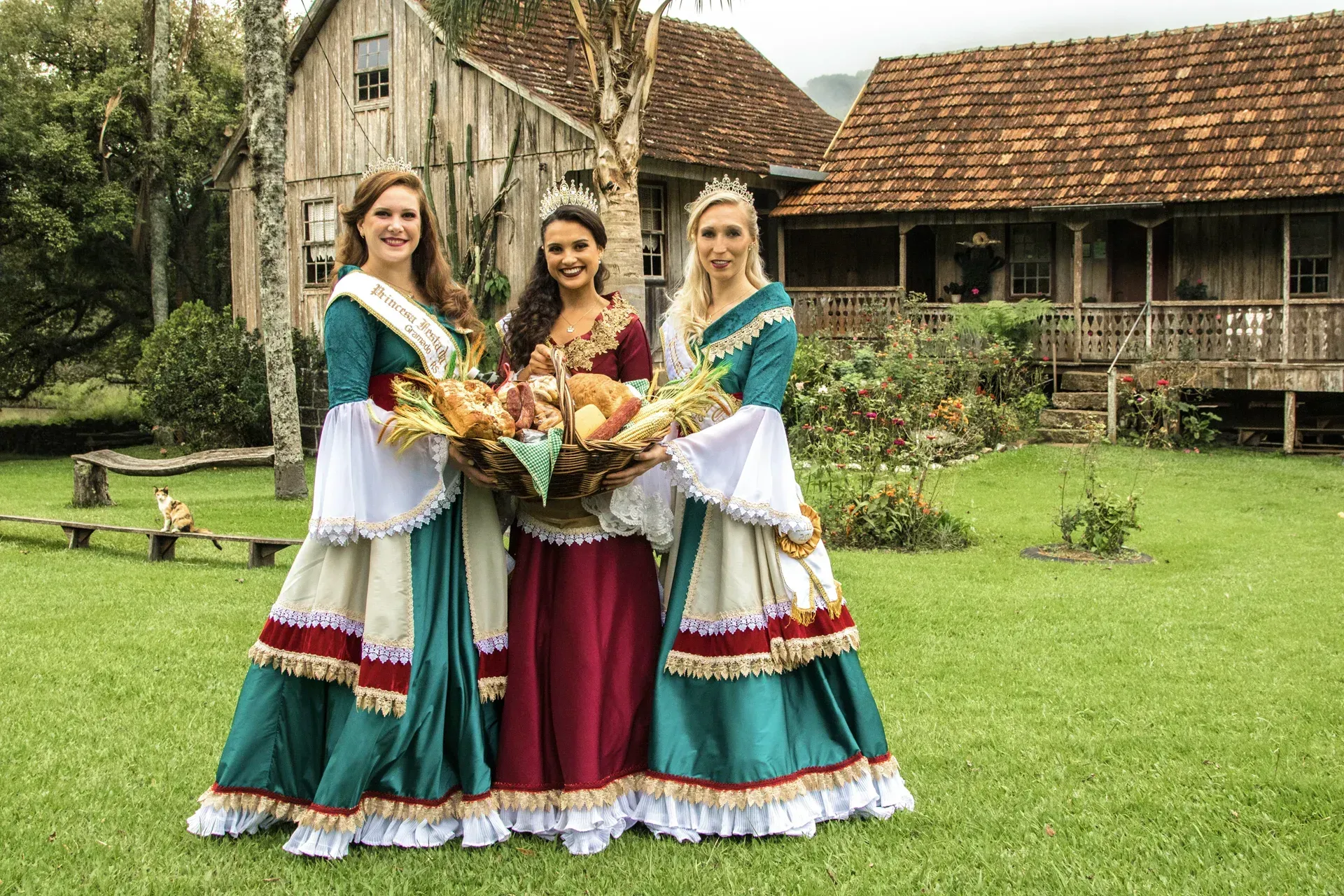 Três mulheres em trajes tradicionais estão posando para uma foto em frente a uma casa de madeira.