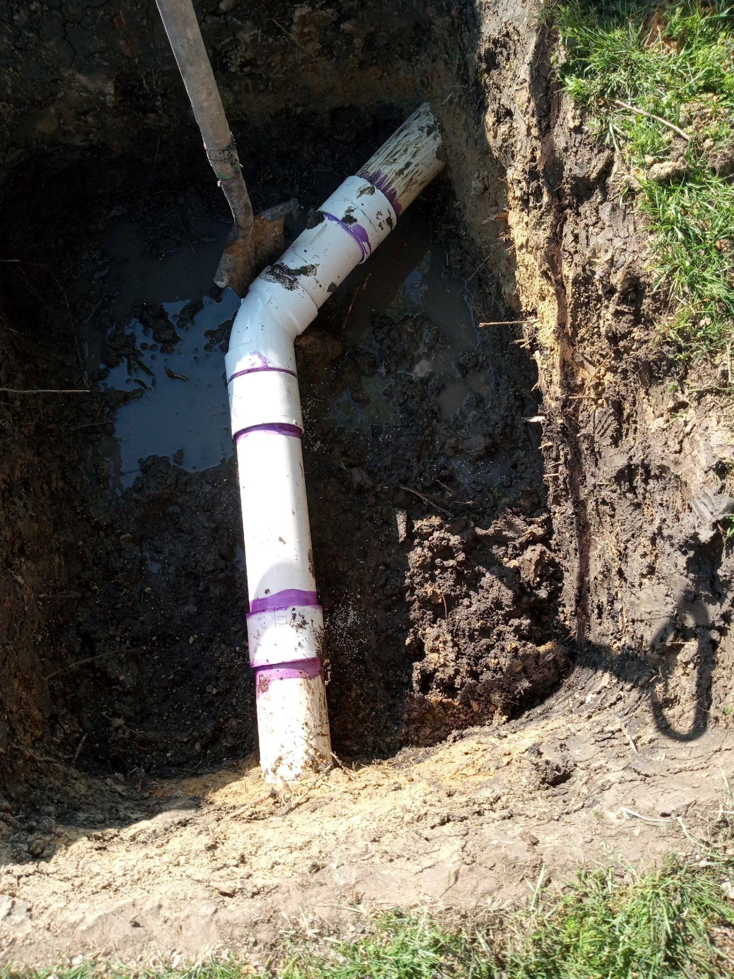 Woman in straw hat smiles, holding wine glass near a lake.