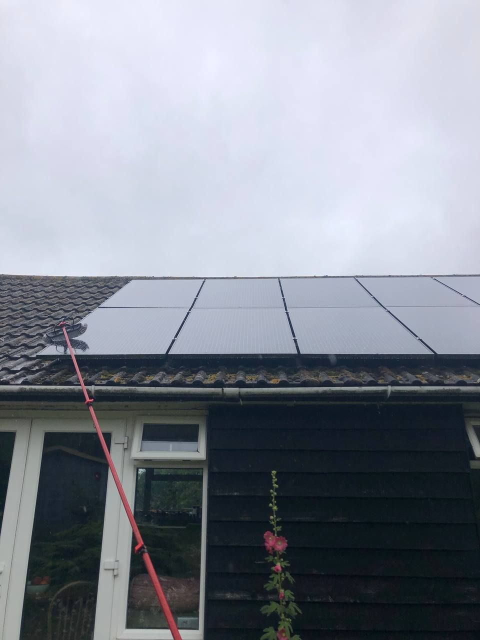 Person cleaning solar panels on a roof with a long-handled brush. The sky is overcast.