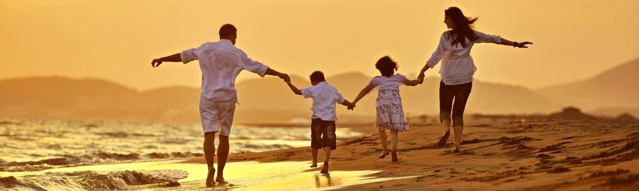 Family running on a beach at sunset, arms outstretched, enjoying time together.