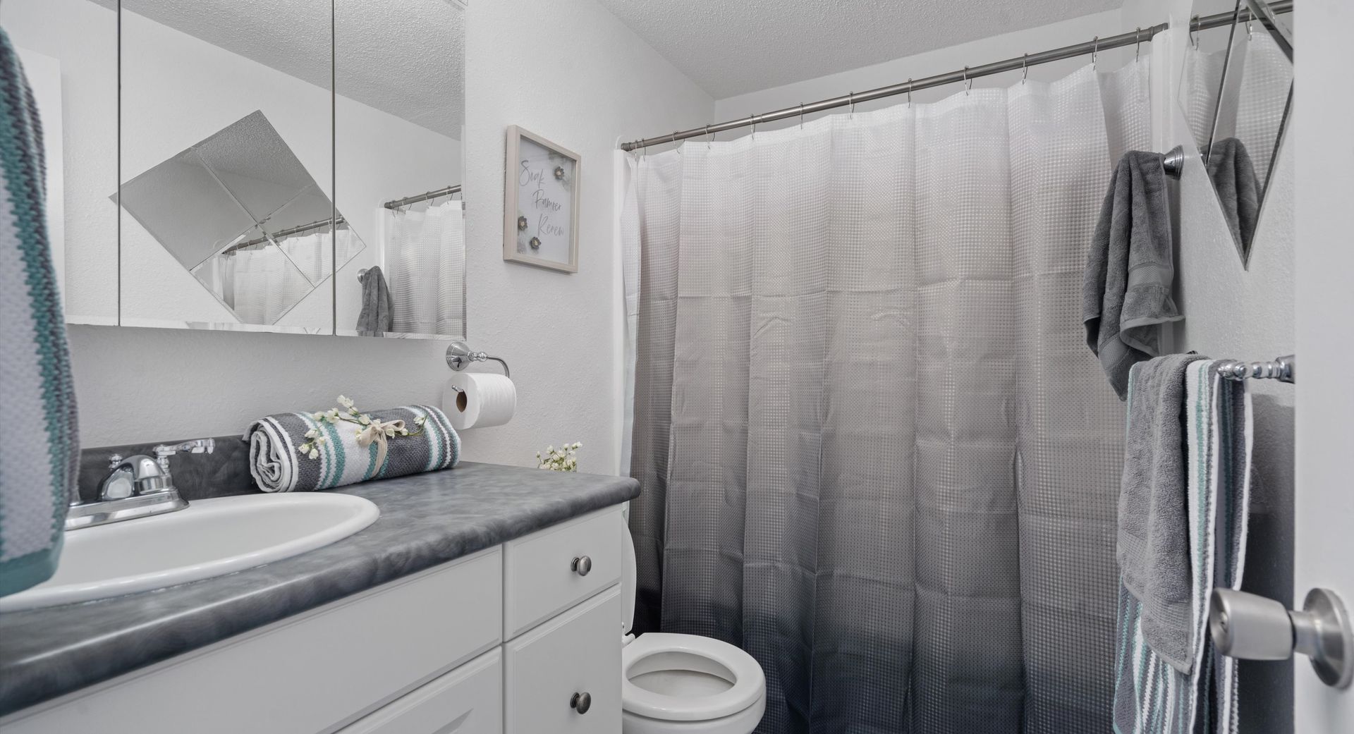 A bathroom with a toilet , sink , mirror and shower curtain.