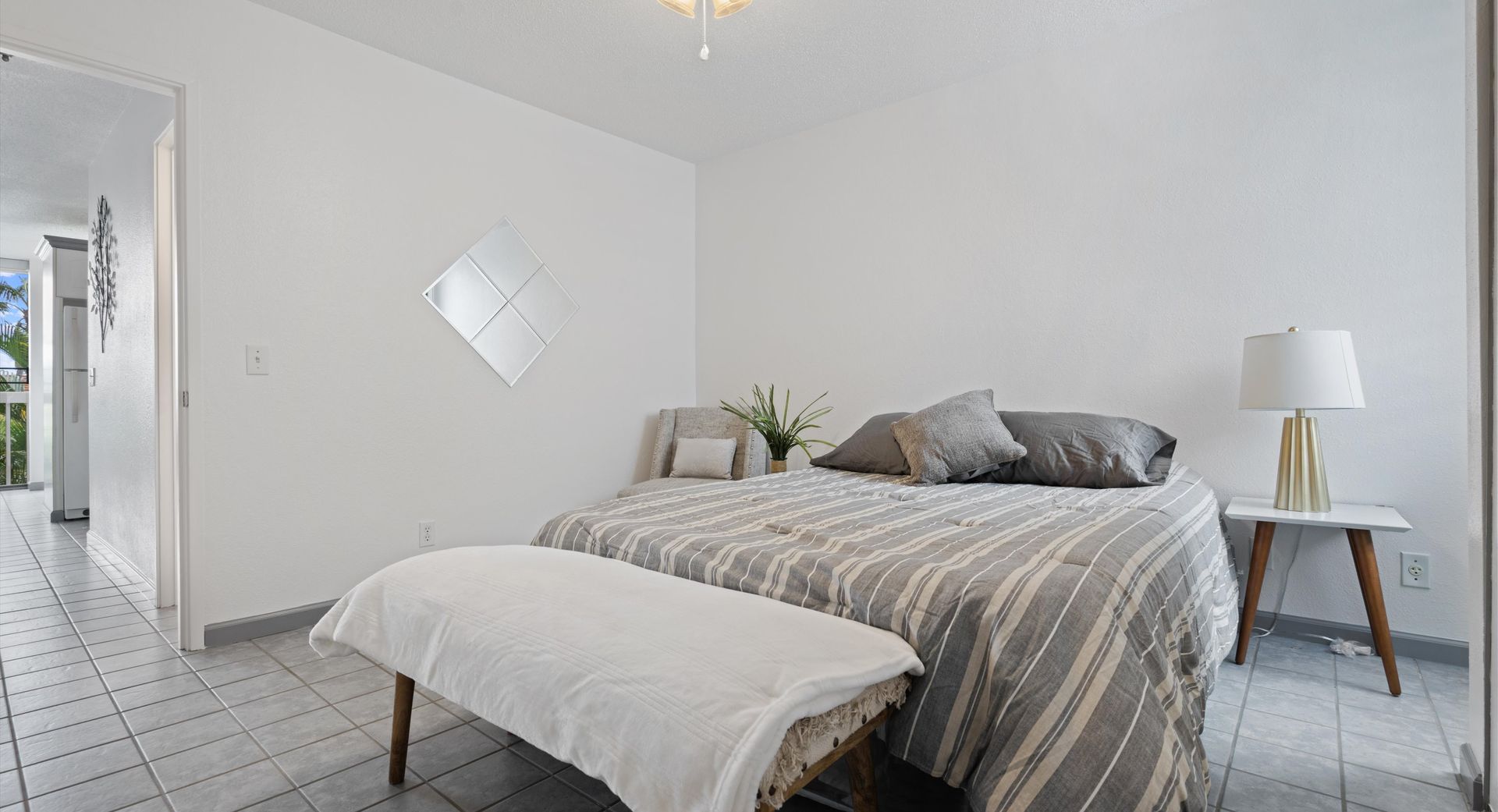 A bedroom with a bed , bench , lamp and mirror.