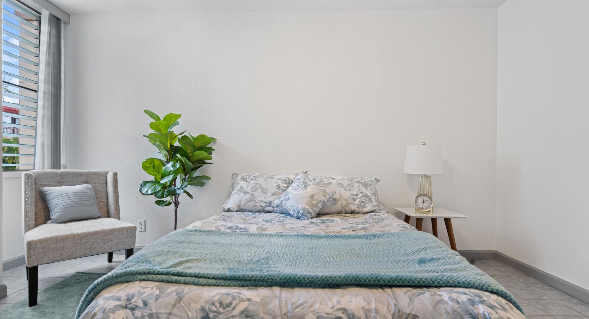 A bedroom with a bed , chair , lamp and window.