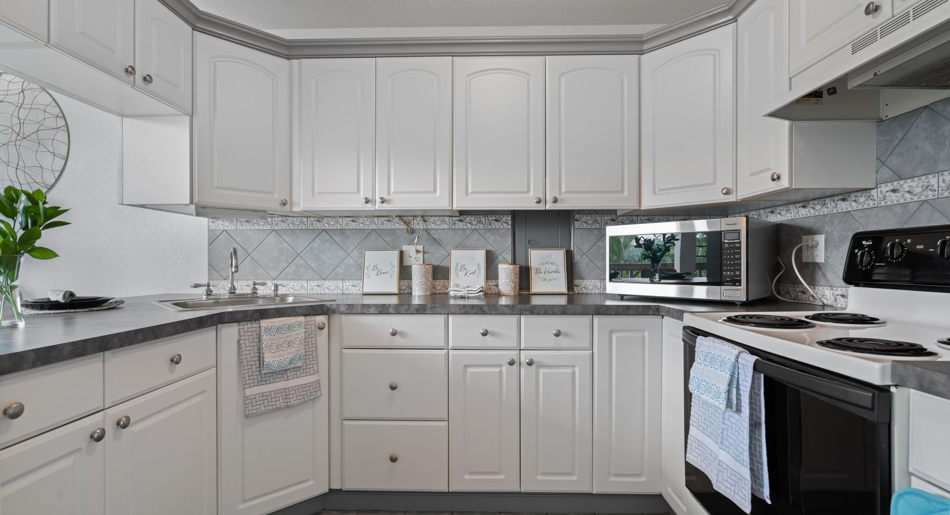 A kitchen with white cabinets , a stove , a microwave , and a sink.