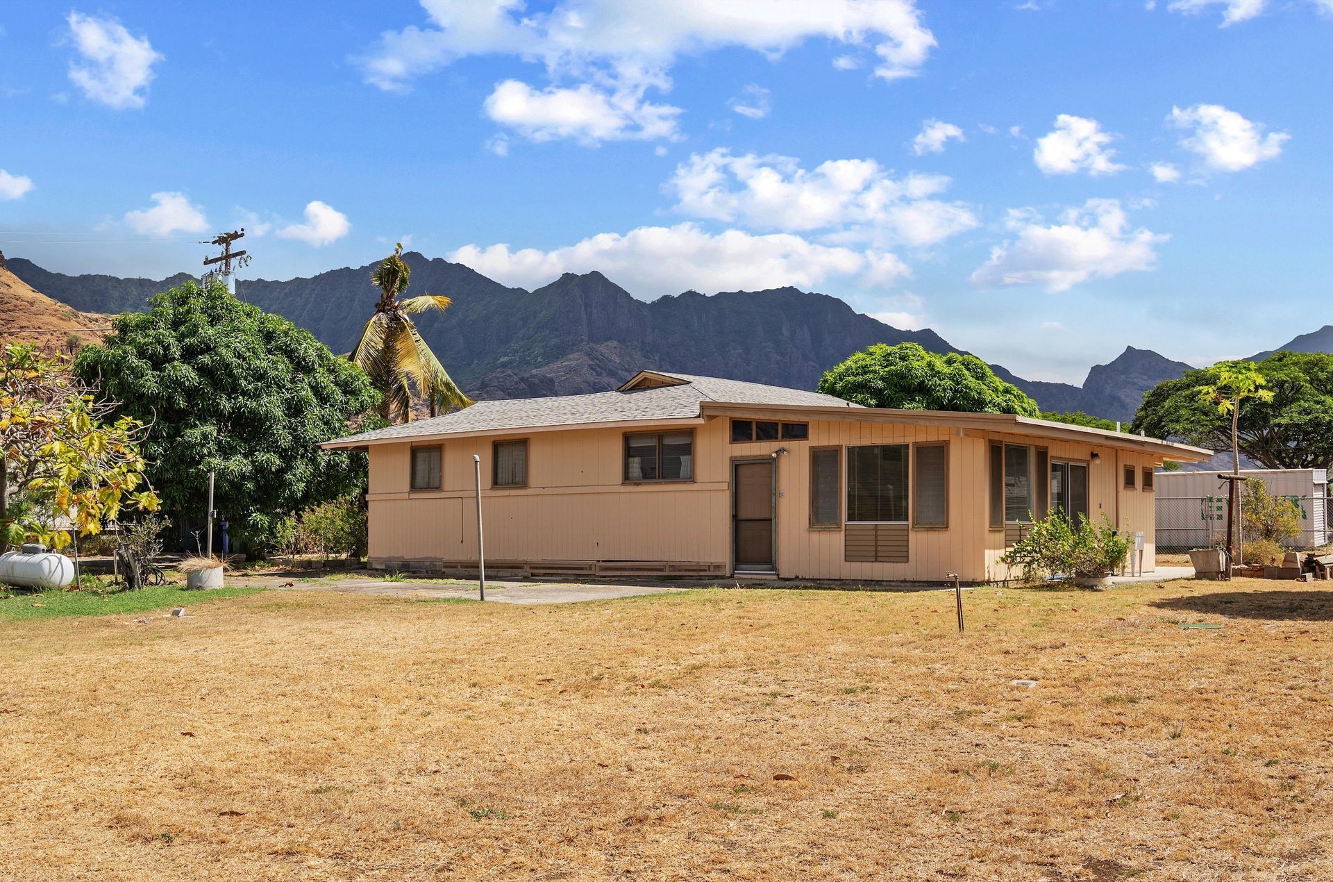 A house is sitting in the middle of a dry field with mountains in the background.