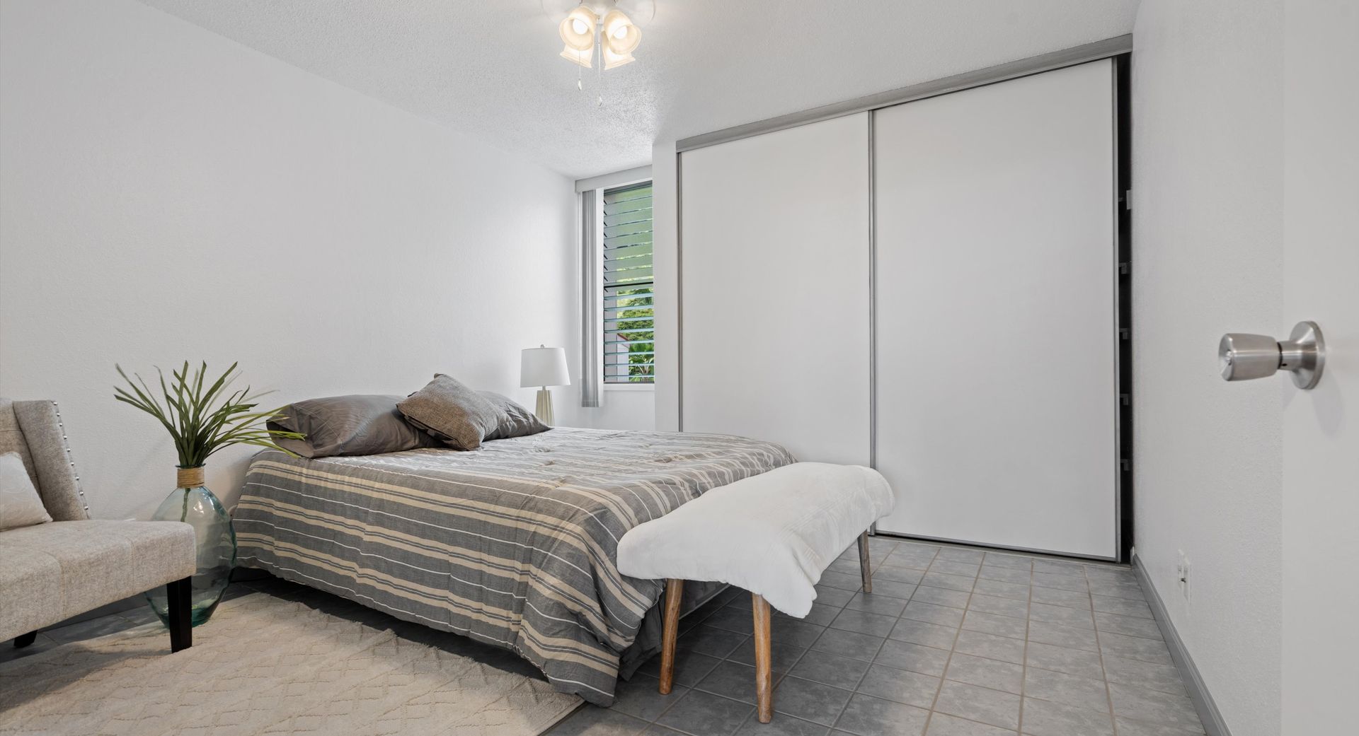 A bedroom with a bed , chair , bench and sliding glass doors.