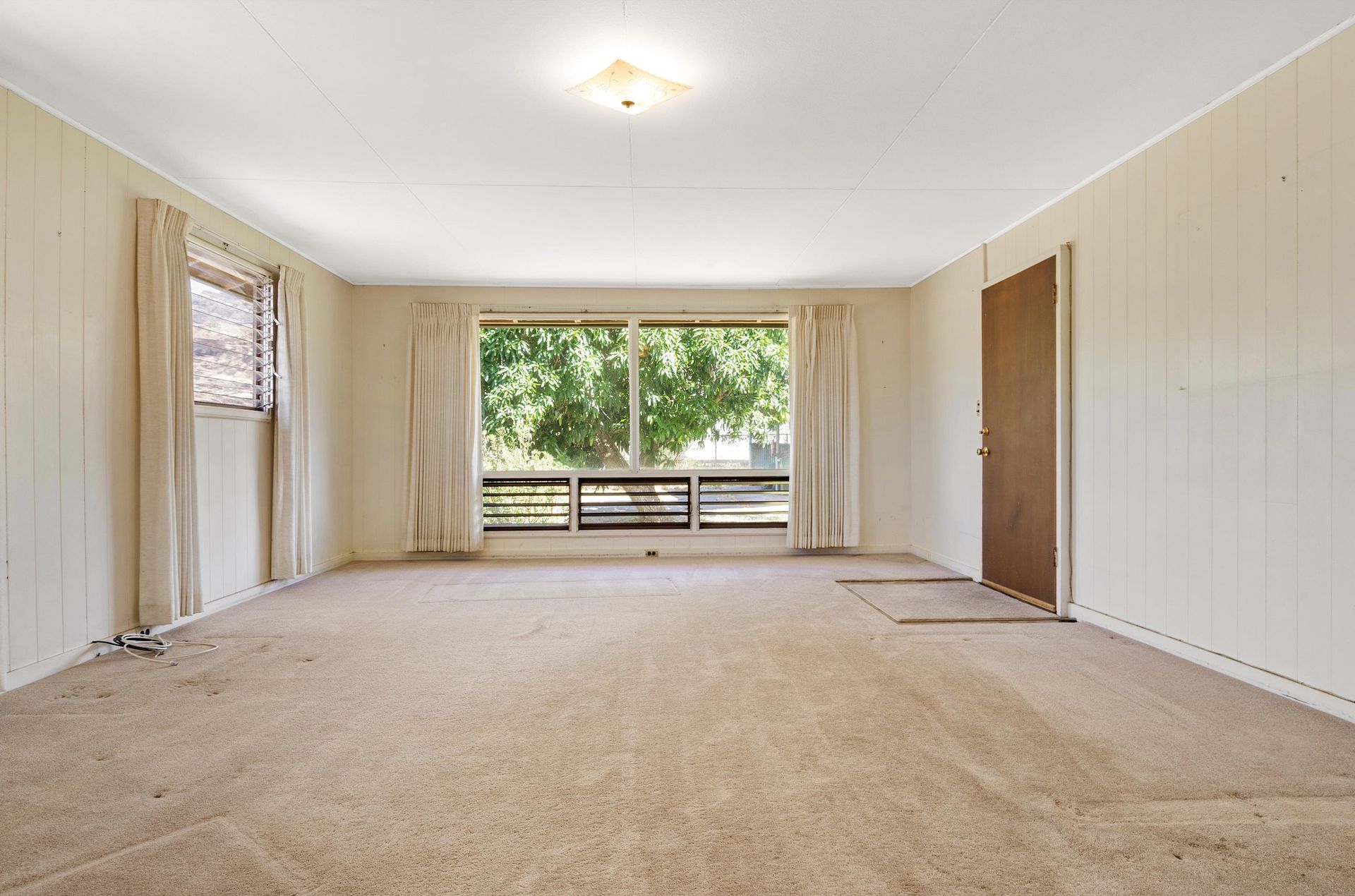 An empty living room with a carpeted floor and a window