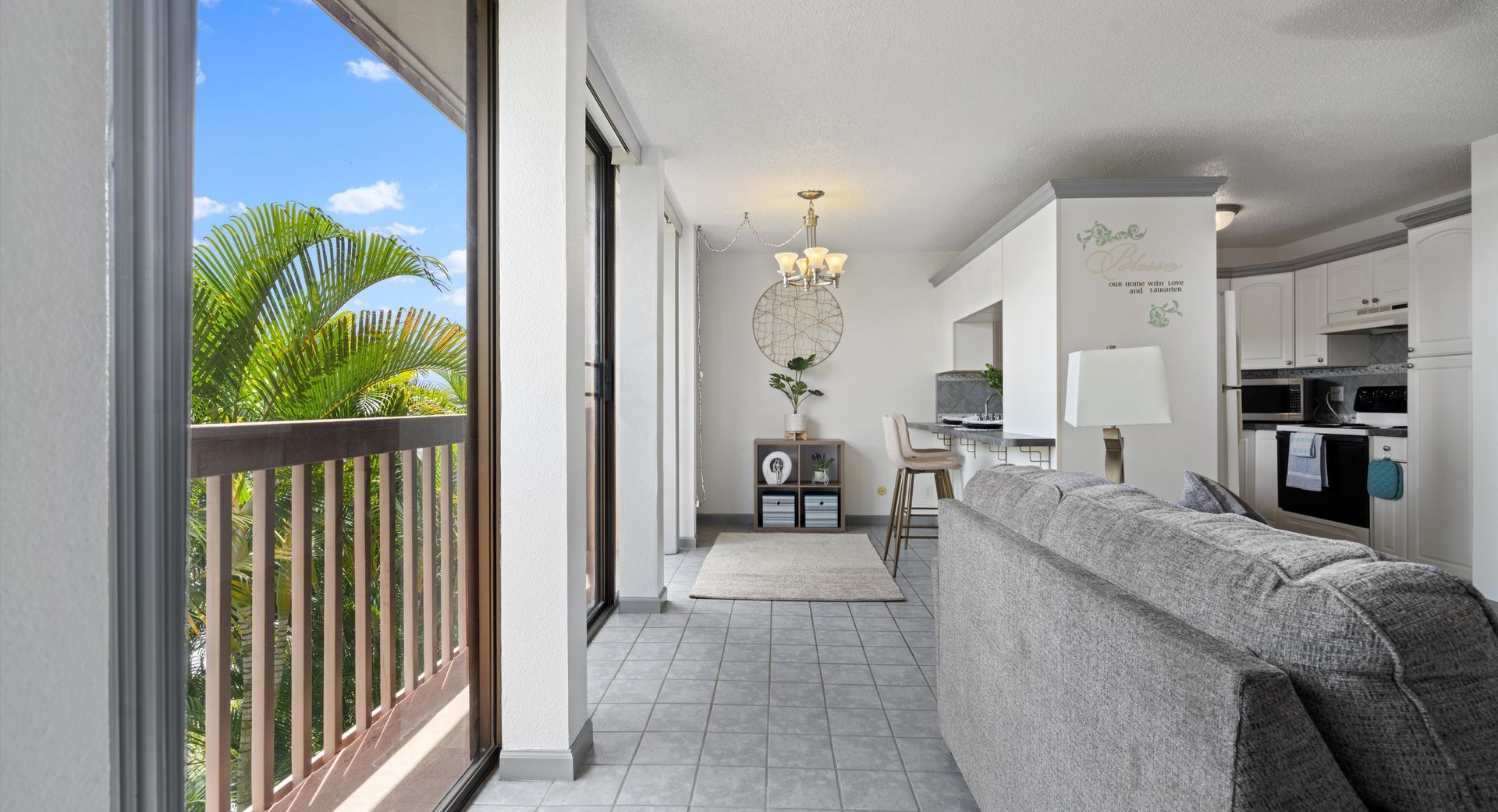 A living room with a couch and a balcony with a view of a palm tree.