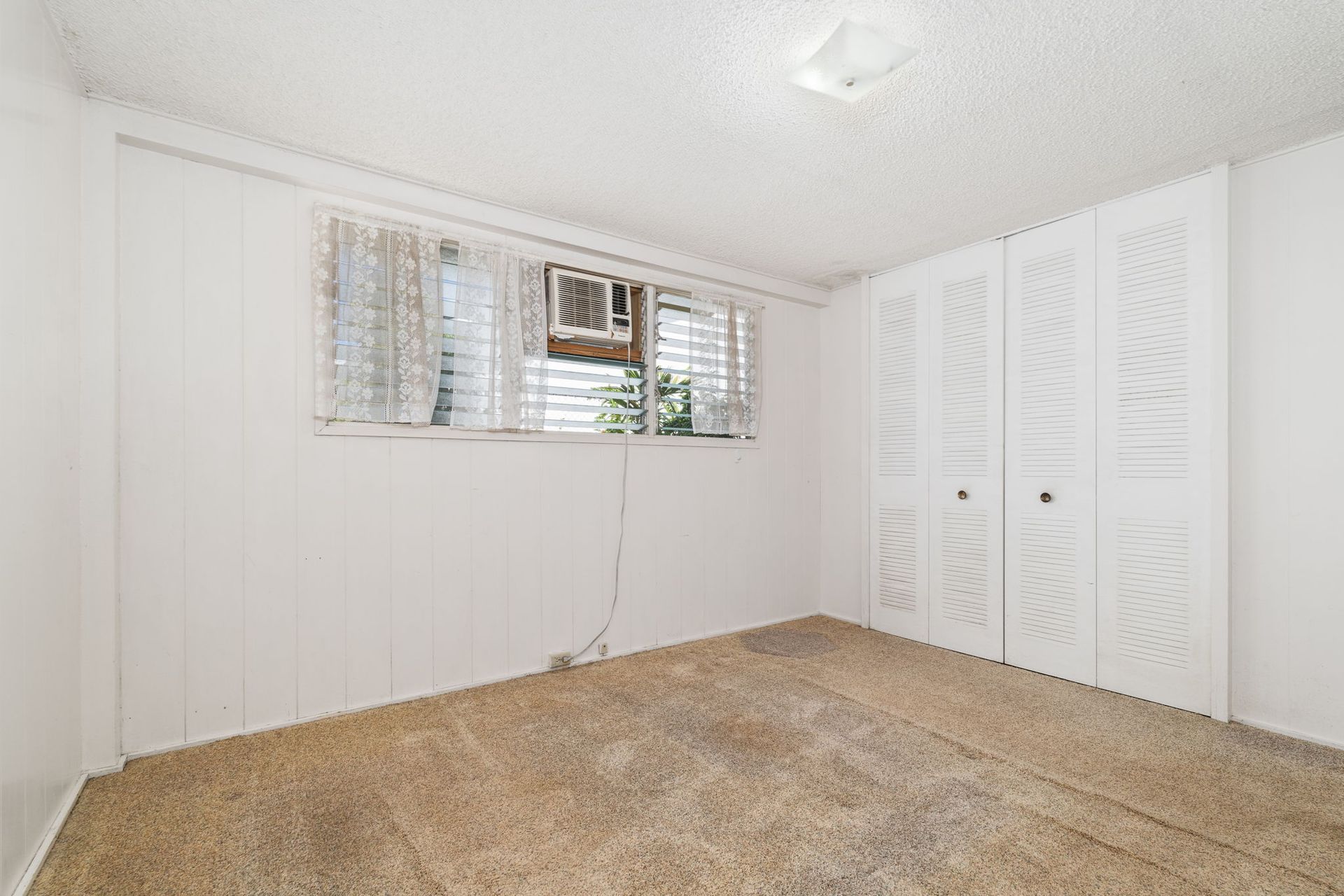 An empty bedroom with a window and closets.