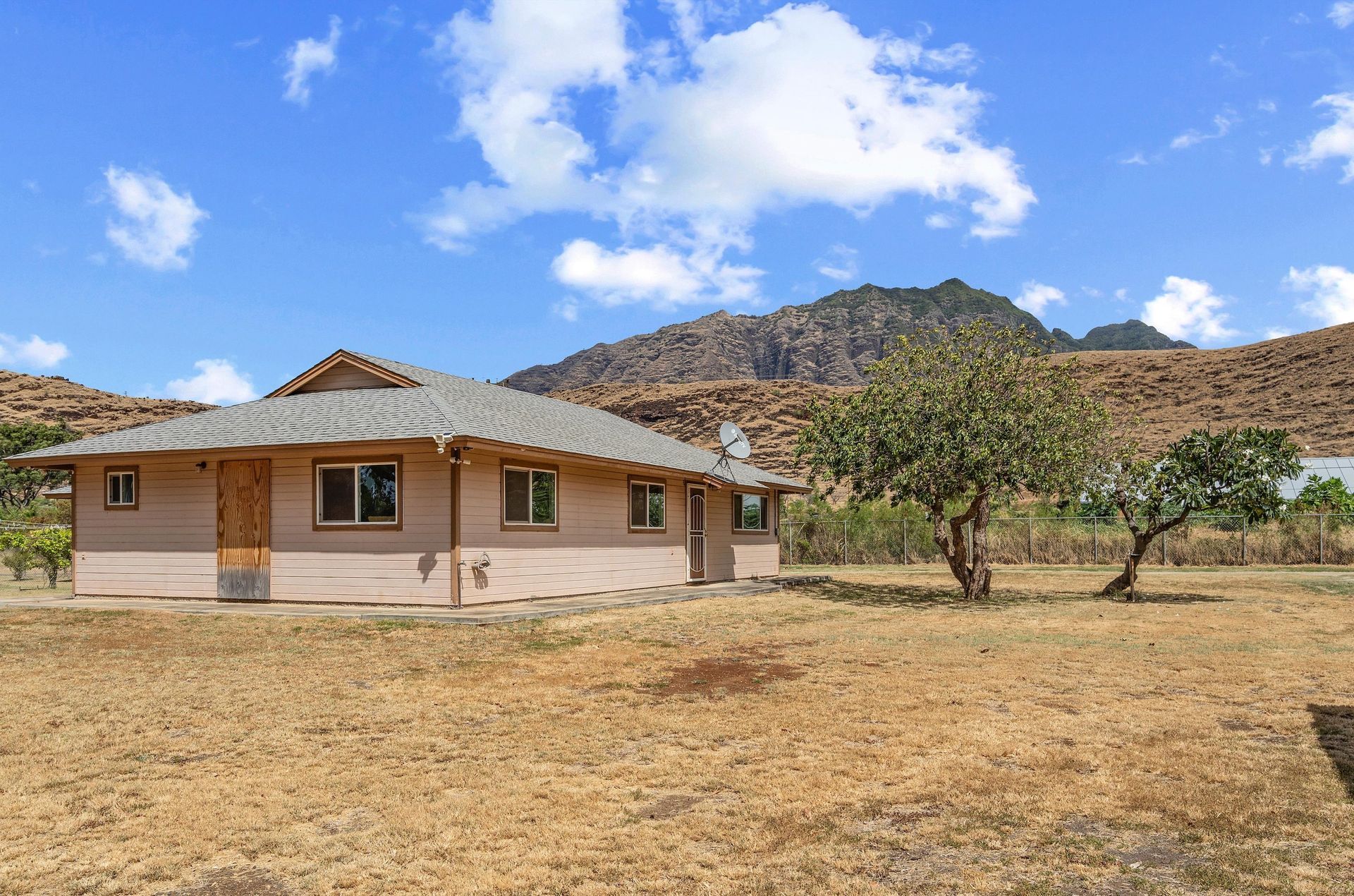 A house is sitting in the middle of a dry field with mountains in the background.
