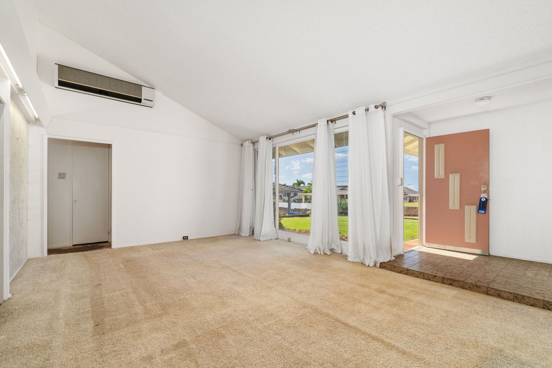 An empty living room with a vaulted ceiling and a ladder hanging from the ceiling.
